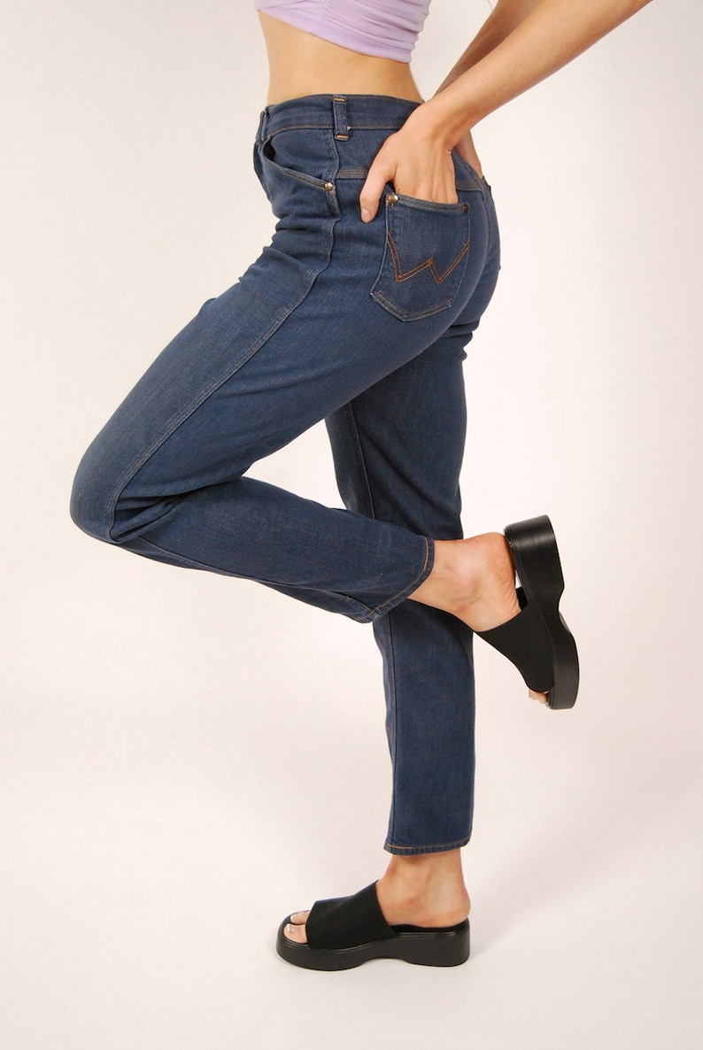 May include: Dark blue denim jeans with a classic five-pocket design. The jeans feature a straight leg cut and a copper-colored stitching detail on the back pockets. Paired with black platform sandals.
