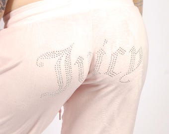May include: Light pink velour sweatpants featuring the word Juicy written in silver rhinestones across the back. The pants have an elastic waistband and a drawstring closure, providing a soft texture and a fitted appearance on the lower body.