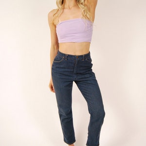 May include: A woman wearing a light purple tube top, dark blue jeans, and black platform sandals. The jeans are high-waisted and straight-legged. The sandals have a thick sole. The woman has long blonde hair.