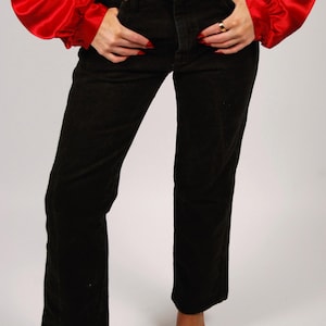 May include: Black corduroy pants with a straight leg, paired with a red satin blouse. The pants have a classic five-pocket design. The outfit is completed with black heeled sandals.