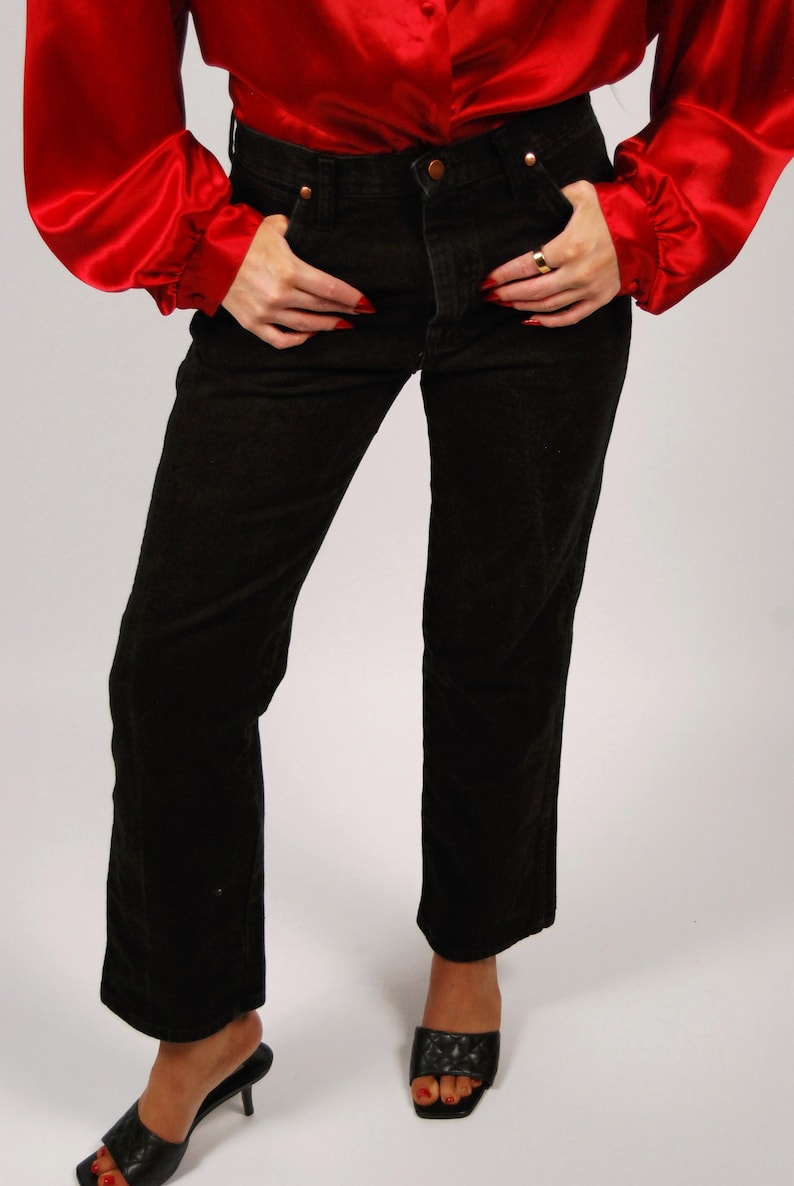 May include: Black corduroy pants with a straight leg, paired with a red satin blouse. The pants have a classic five-pocket design. The outfit is completed with black heeled sandals.