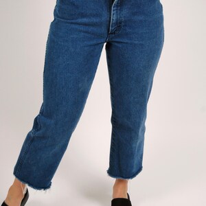Op de afbeelding: Blauwe jeans van denim met een hoge taille en een rechte pijp. De jeans hebben een gerafelde zoom en een klassiek ontwerp met vijf zakken. Het model draagt ​​zwarte sandalen.