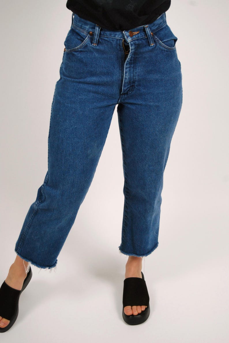 Op de afbeelding: Blauwe jeans van denim met een hoge taille en een rechte pijp. De jeans hebben een gerafelde zoom en een klassiek ontwerp met vijf zakken. Het model draagt ​​zwarte sandalen.