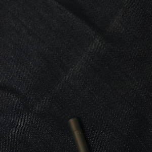 May include: Close-up of dark blue denim fabric with a subtle texture. A dark gray pen is in the lower right corner, providing a sense of scale and contrast against the denim.