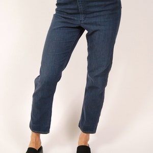 May include: Dark wash denim jeans with a high waist and straight leg. The jeans have a classic five-pocket design and a button and zipper closure. The model is wearing black platform sandals.
