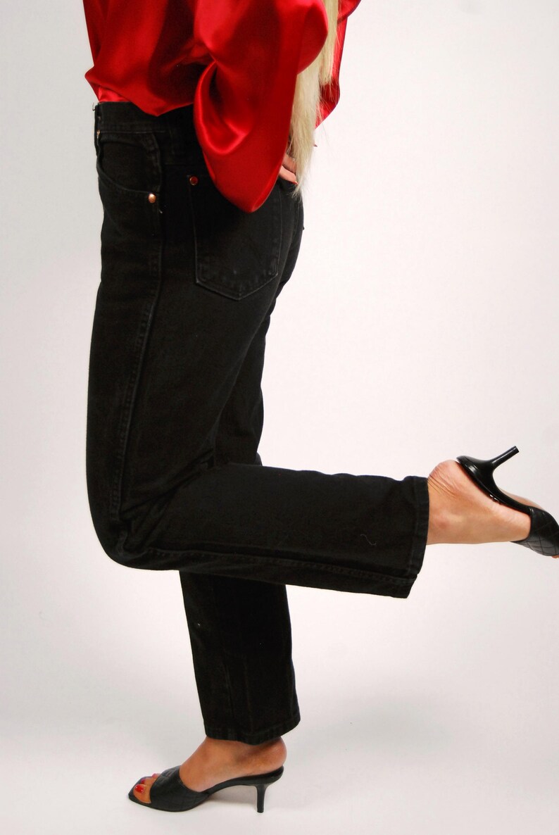 May include: Black denim jeans with a classic five-pocket design. The jeans are paired with black heeled mules and a red satin top. The jeans have a straight leg cut and a button and zipper closure.