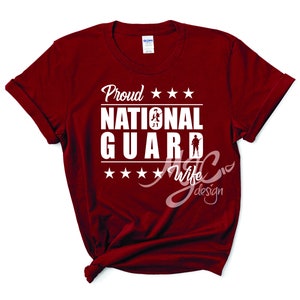 May include: Red t-shirt with white text that reads "Proud National Guard Wife". The text is surrounded by five white stars.