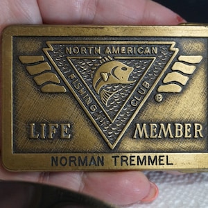 May include: A gold-colored metal belt buckle with the text "North American Fishing Club" and "Life Member" and the name "Norman Tremmel".