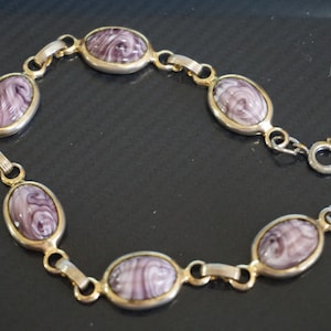 May include: A gold chain bracelet with purple oval-shaped stones. The stones have a swirling pattern.