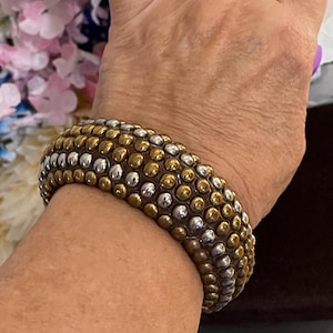 May include: A gold and silver studded bangle bracelet. The bracelet is made of a smooth, rounded material and has a textured surface.