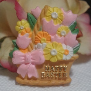 May include: A pink and yellow ceramic Easter basket with a bow and flowers. The basket has the words "Happy Easter" written on it.