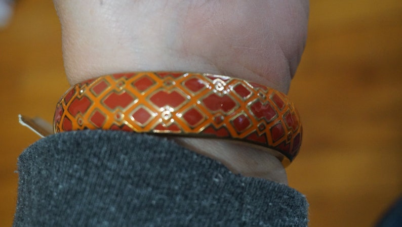 May include: A gold bangle bracelet with a red and orange geometric pattern.