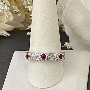 May include: A silver band ring with five red gemstones set in a decorative pattern.