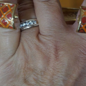 May include: A hand wearing a ring with clear stones and two orange and gold bracelets with a geometric pattern.