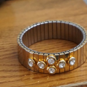 May include: A gold and silver expandable bracelet with a row of clear rhinestones.