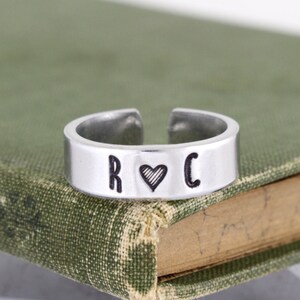 Peut inclure: Une bague en argent avec les lettres "R" et "C" de chaque côté d'un symbole de cœur.