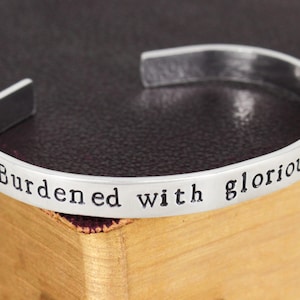 May include: Silver bracelet with the inscription "Burdened with glorious p..."