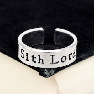 May include: A silver adjustable ring with the words "Sith Lord" engraved on the band.