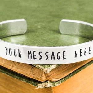 May include: Silver bracelet with the text "YOUR MESSAGE HERE" engraved on it.