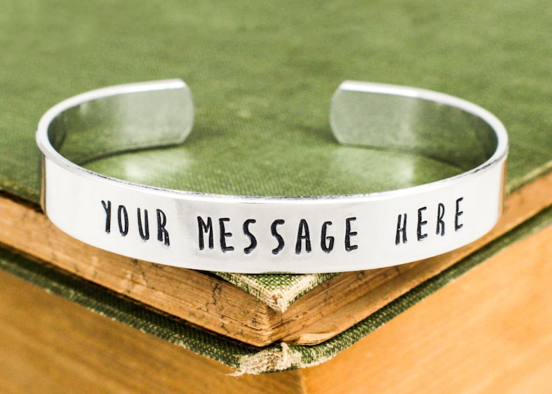 May include: Silver bracelet with the text "YOUR MESSAGE HERE" engraved on it.