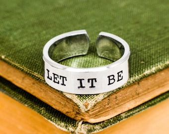 Puede incluir: Un anillo ajustable de plata con las palabras "LET IT BE" grabadas en la banda.