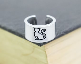 May include: Silver bookmark with a black silhouette of a cat sitting on a book.