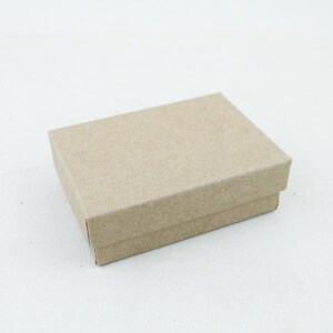 Puede incluir: Una pequeña caja rectangular cerrada de cartón. La caja es de color marrón claro y tiene un diseño simple y limpio. La caja probablemente se utiliza para empaquetar artículos pequeños, como joyas o regalos.