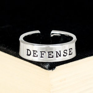 May include: A silver ring with the word "DEFENSE" engraved on it.