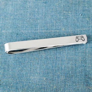 May include: Silver tie bar with a black engraved video game controller design.