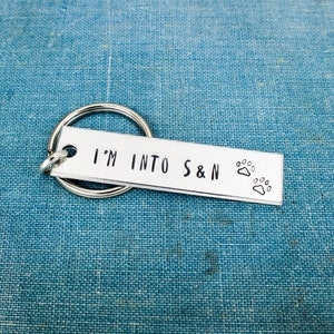 May include: Silver keychain with a rectangular tag that reads "I'm into S&N" with two paw prints.
