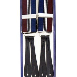 Puede incluir: Un par de tirantes con correas elásticas a rayas burdeos, azul marino y blanco y extremos de cuero negro. Los tirantes están empaquetados en una caja azul con la palabra "Revival" y "Made in England" impresa en ella.