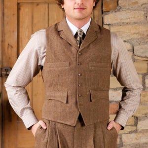 May include: A brown tweed three-piece suit, comprising a waistcoat, trousers, and a collared shirt with a patterned tie. The waistcoat features two front pockets and a button closure. The trousers are pleated. The shirt has a striped pattern.