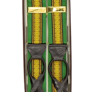 May include: Green and gold patterned suspenders with black leather attachments and gold-colored metal clasps. The suspenders are presented in a brown box, showcasing a classic accessory.