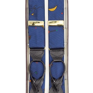 Può includere: Bretelle blu con un motivo di lune crescenti gialle e forme colorate. Le bretelle hanno chiusure in metallo dorato e passanti in pelle nera. Sono presentate in una scatola marrone.