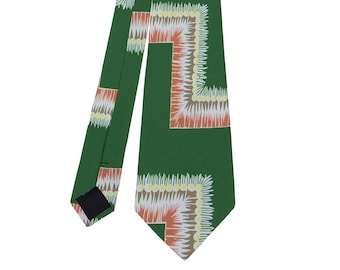 May include: A green tie with a white and orange geometric pattern. The pattern is made up of repeating squares with a floral design.