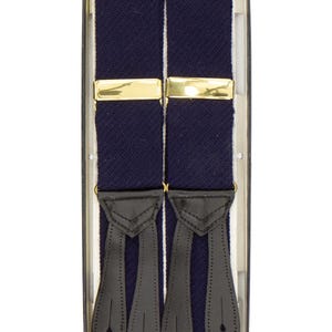Puede incluir: Tirantes azul marino con cierres metálicos dorados y extremos de cuero negro, presentados en una caja transparente. Un accesorio clásico para vestimenta formal o de negocios. Miden aproximadamente 100 cm de largo.