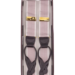 May include: A pair of suspenders with a red and white striped pattern, gold-colored clasps, and black leather attachments. The suspenders are presented in a rectangular box with a dark burgundy border.