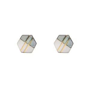 Puede incluir: Un par de pendientes de botón hexagonales con un diseño geométrico. Cada pendiente está dividido en secciones de piedra blanca y verde pálido, separadas por finas líneas metálicas doradas verticales que atraviesan la superficie del hexágono.