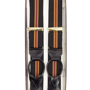 May include: Black suspenders with gold-tone clasps and leather loops, presented in a box. The suspenders feature vertical stripes in black, gold, and red. The suspenders are a classic accessory for trousers.
