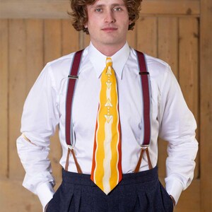 May include: A crisp white long-sleeved button-down shirt paired with dark charcoal pleated trousers. The outfit features a vibrant yellow necktie with a white geometric pattern and burgundy braces with silver hardware and brown leather tabs.