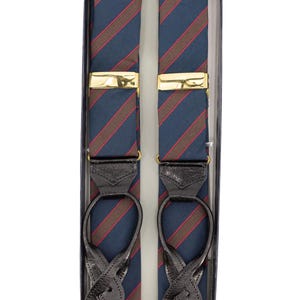 Puede incluir: Tirantes a rayas azules y rojas con cierres dorados y detalles de cuero negro, presentados en una caja azul marino. Diseño clásico para un estilo elegante.