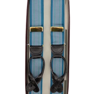 Può includere: Bretelle a righe blu e verdi con attacchi in pelle nera e chiusure in metallo color oro, presentate in una scatola marrone. Le bretelle hanno un design classico, adatto per occasioni formali.