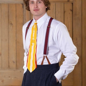 May include: A crisp white long-sleeved button-down shirt paired with dark charcoal trousers, burgundy braces with light blue stripes, and a bright yellow necktie featuring a white geometric pattern and wavy vertical lines.