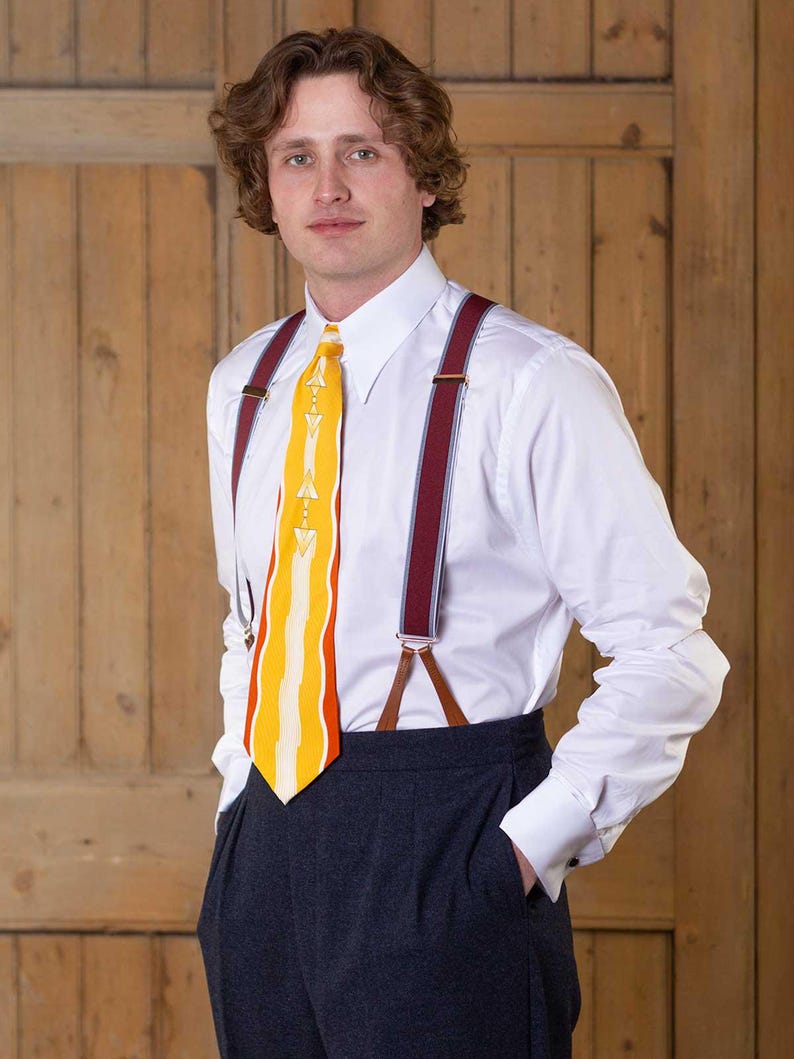 May include: A crisp white long-sleeved button-down shirt paired with dark charcoal trousers, burgundy braces with light blue stripes, and a bright yellow necktie featuring a white geometric pattern and wavy vertical lines.