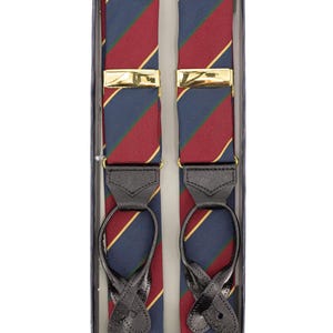 Puede incluir: Tirantes con un diseño a rayas azul marino, rojo y dorado, presentados en una caja transparente. Cuentan con cierres metálicos dorados y enganches de cuero negro. Accesorio clásico.