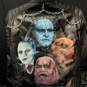 May include: Black leather jacket with a painted design of four characters from the Hellraiser film series. The jacket has a quilted pattern on the shoulders and a silver chain detail across the upper back.