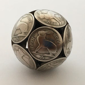 May include: A silver sphere made from multiple Irish 3 pence coins featuring a hare design. The coins are arranged to form a sphere with the hare facing outward on each coin.