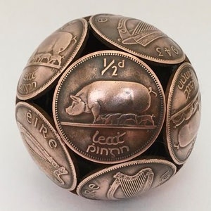 May include: A sphere made of copper-coloured Irish coins. The coins are arranged in a pattern, with the centre coin featuring a pig and the text "1/2d leat phingin".
