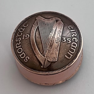 Könnte beinhalten: Eine runde Schmuckdose aus Metall mit einem Deckel aus einer irischen Münze von 1935. Der Deckel zeigt ein Harfenemblem mit dem Text SAORSTÁT ÉIREANN und dem Jahr 1935. Der Boden ist ein glattes, kupferfarbenes Metallband mit verziertem Rand.
