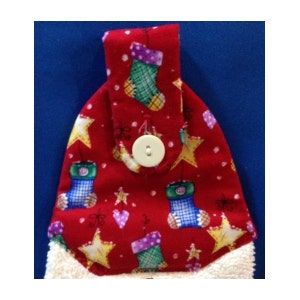 以下が含まれることがあります： 赤色のクリスマスをテーマにした吊り下げタオル。靴下、星、ハートの模様が特徴です。ボタン留めと、柔らかく白いふわふわの裾が付いています。デザインは赤い背景にプリントされています。